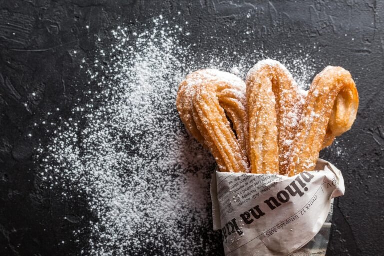 Close-up of freshly baked churros with powdered sugar on newspaper. A tasty dessert treat.
