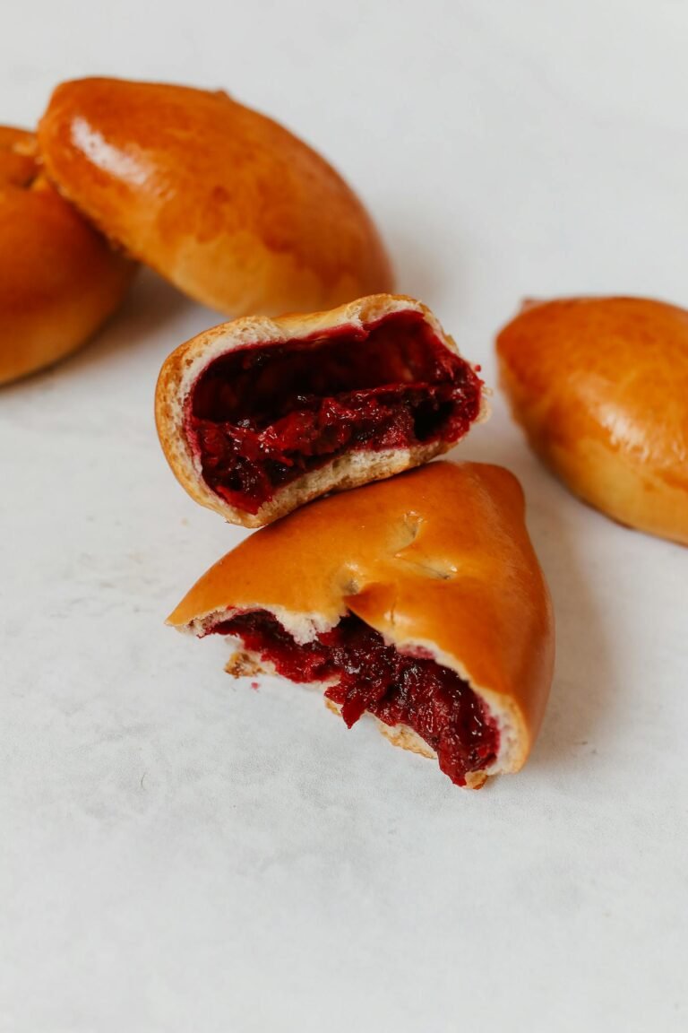 Close-up of freshly baked Russian pirozhki pastries with a sweet, rich filling on a white surface.